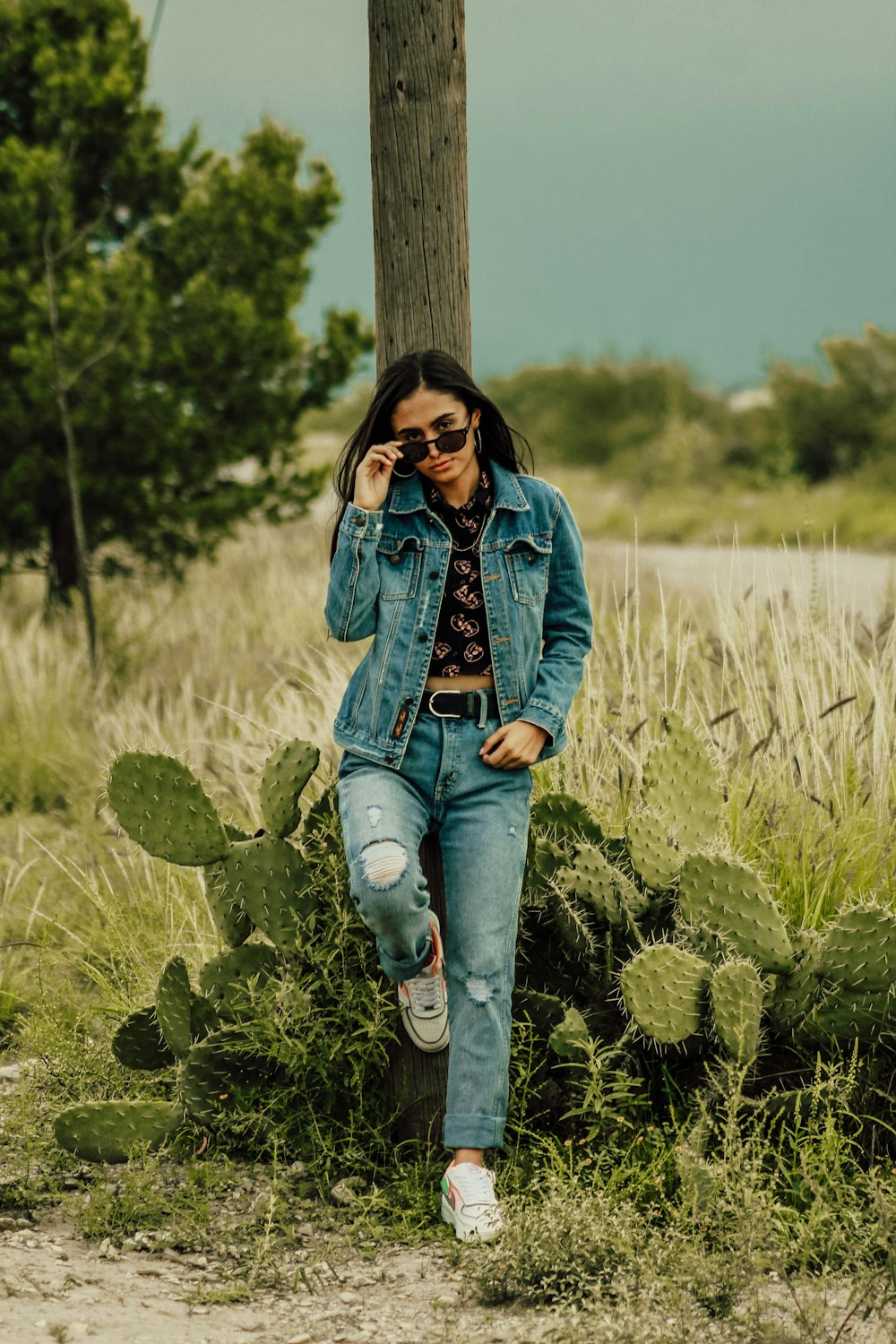 woman in blue denim jacket and blue denim jeans standing beside brown wooden post during daytime