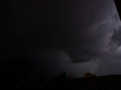 Dark stormy sky with heavy clouds and a visible bolt of lightning illuminating the scene, silhouetting a cityscape in the foreground.