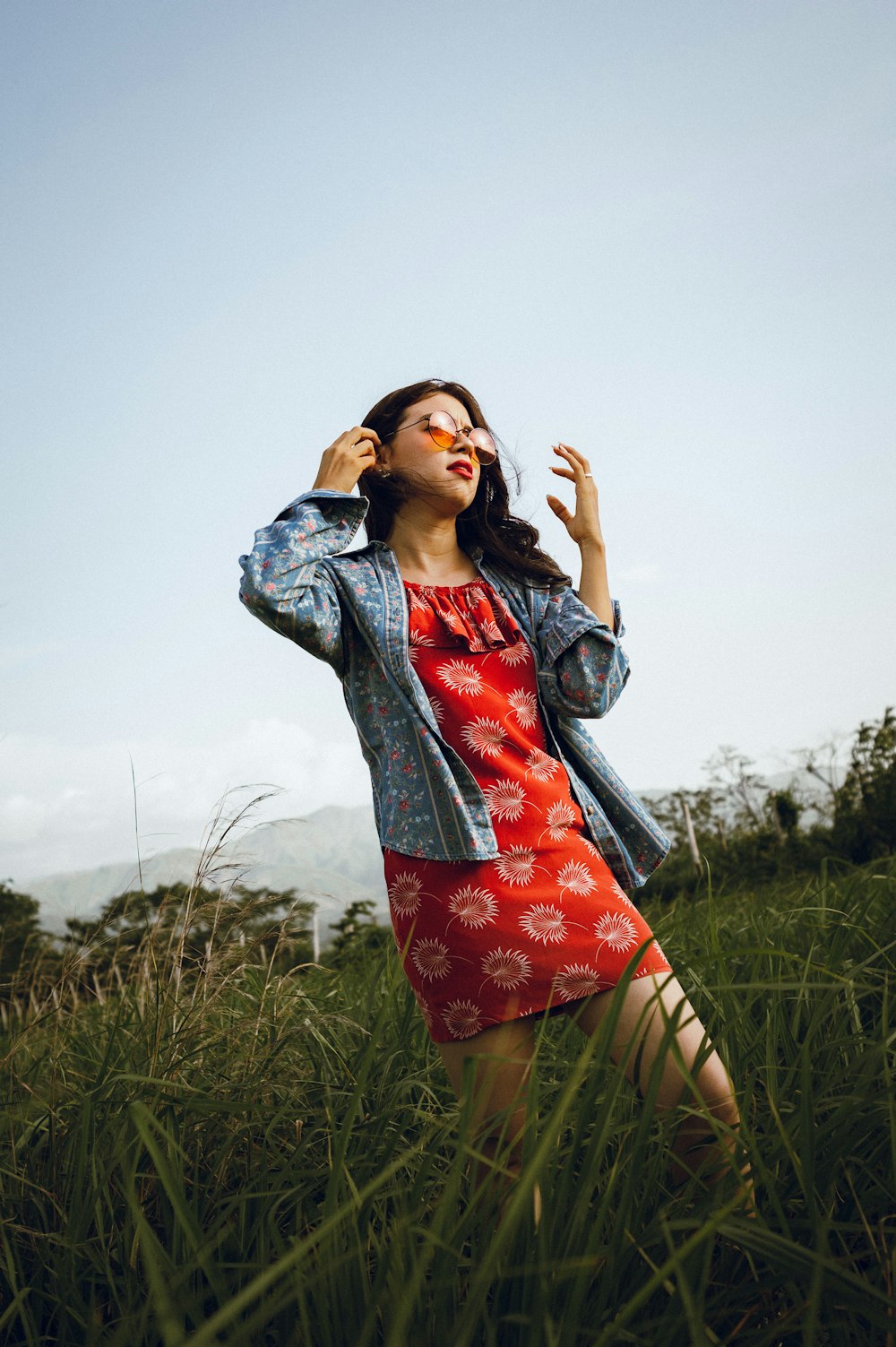 Femme en veste en jean bleue et jupe à fleurs rouge debout sur le champ d’herbe verte pendant la journée