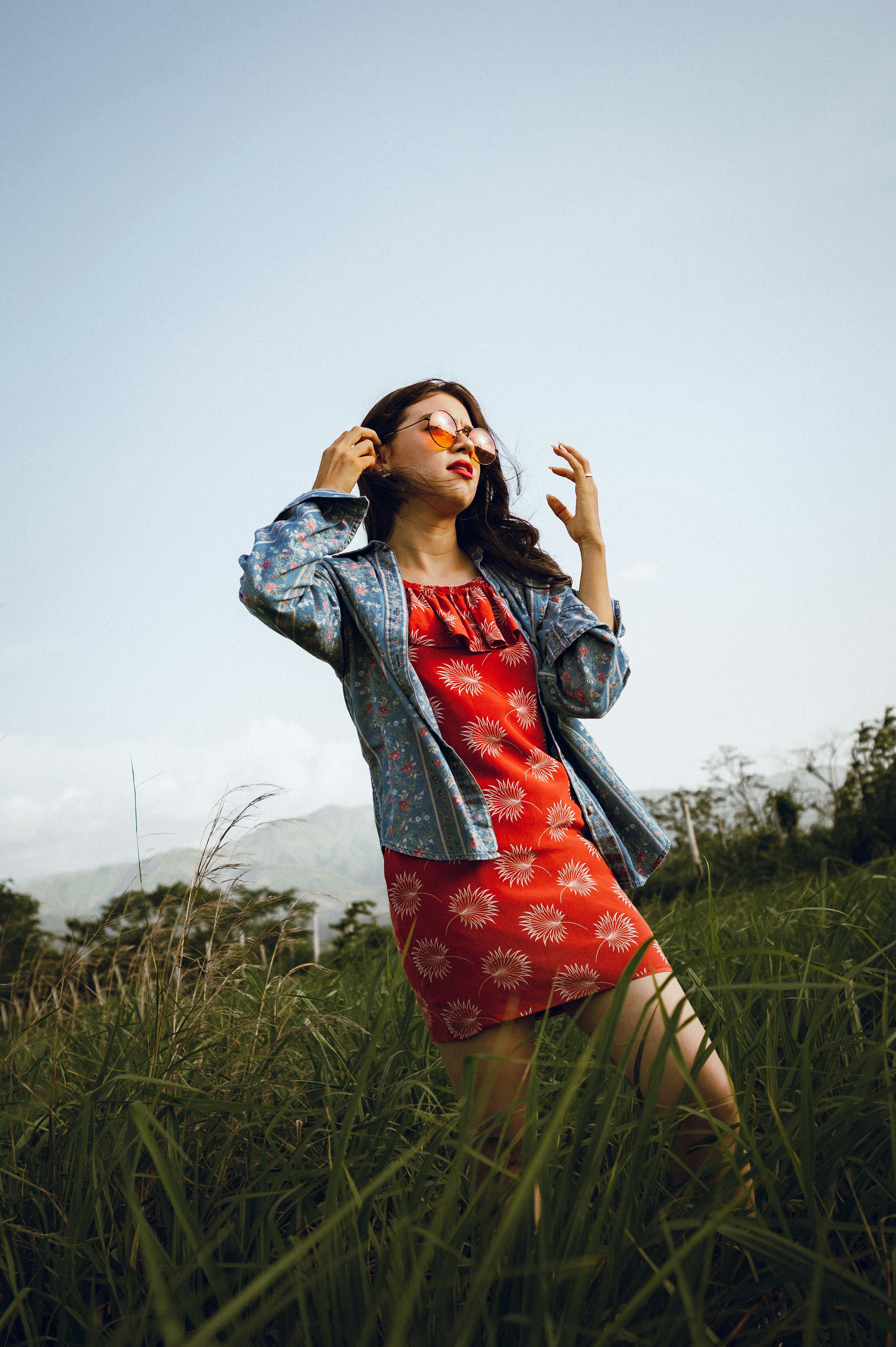 woman in blue denim jacket and red floral skirt standing on green grass field during daytime