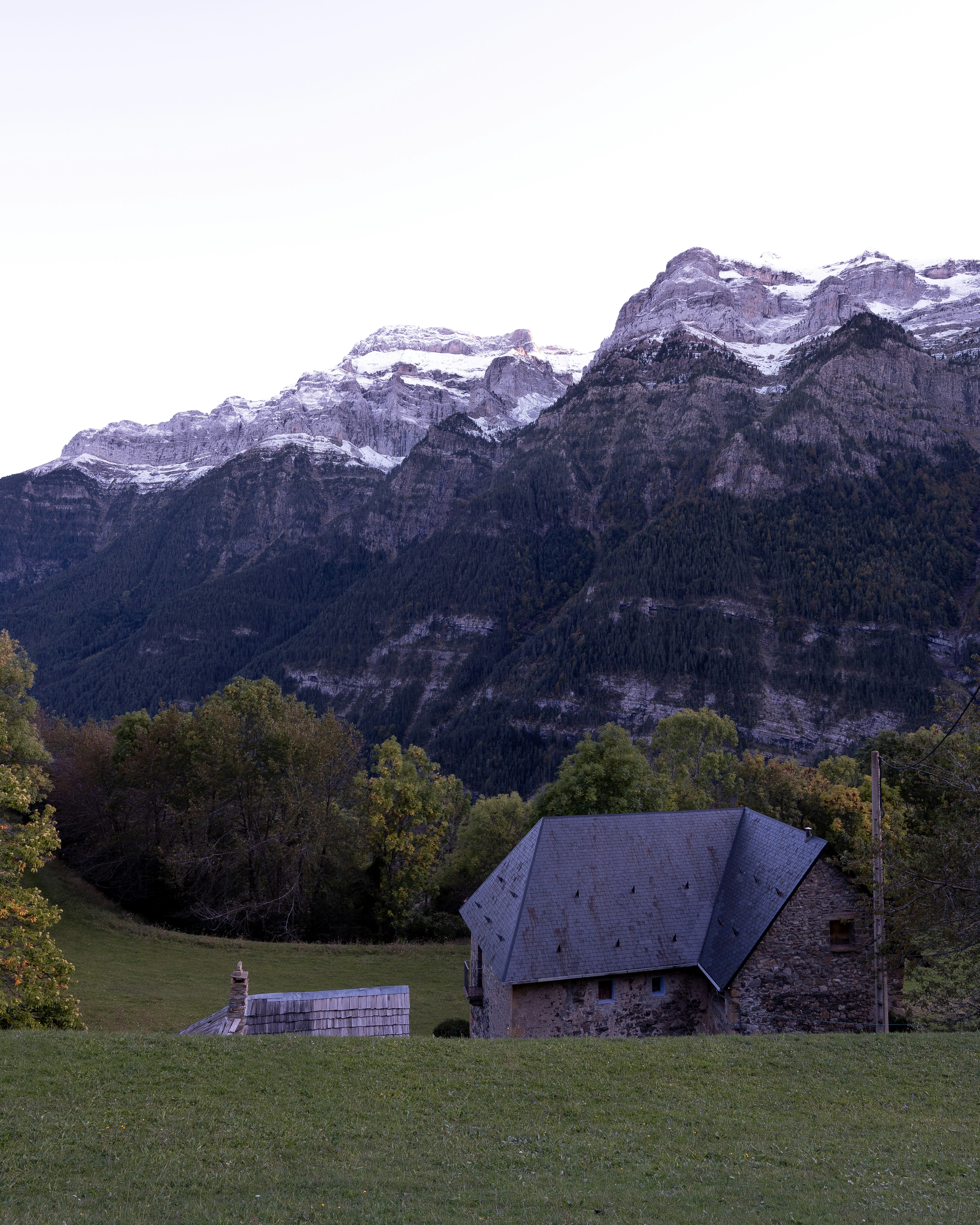 gray wooden house on green grass field near mountain during daytime