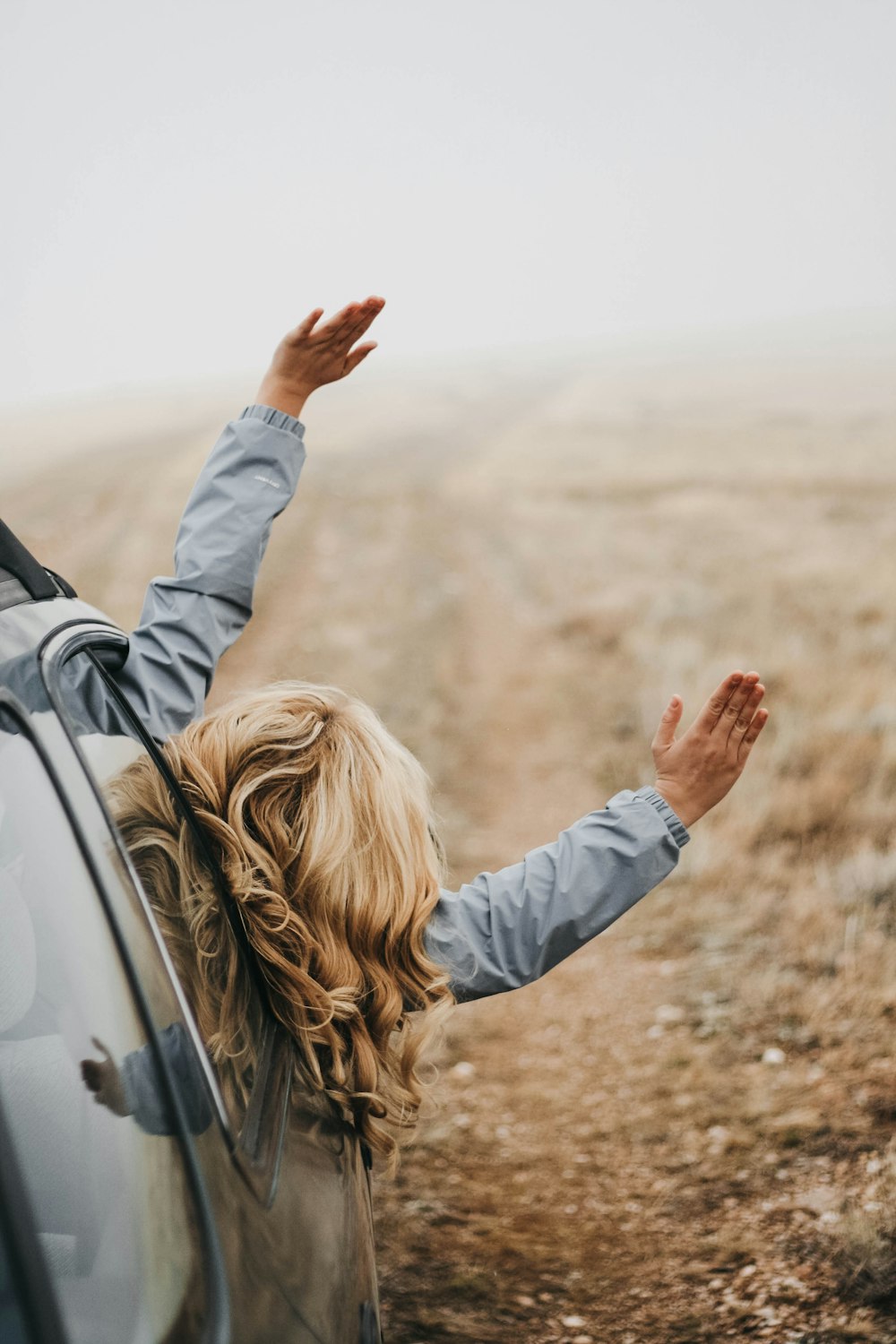 woman in gray jacket leaning on white car during daytime