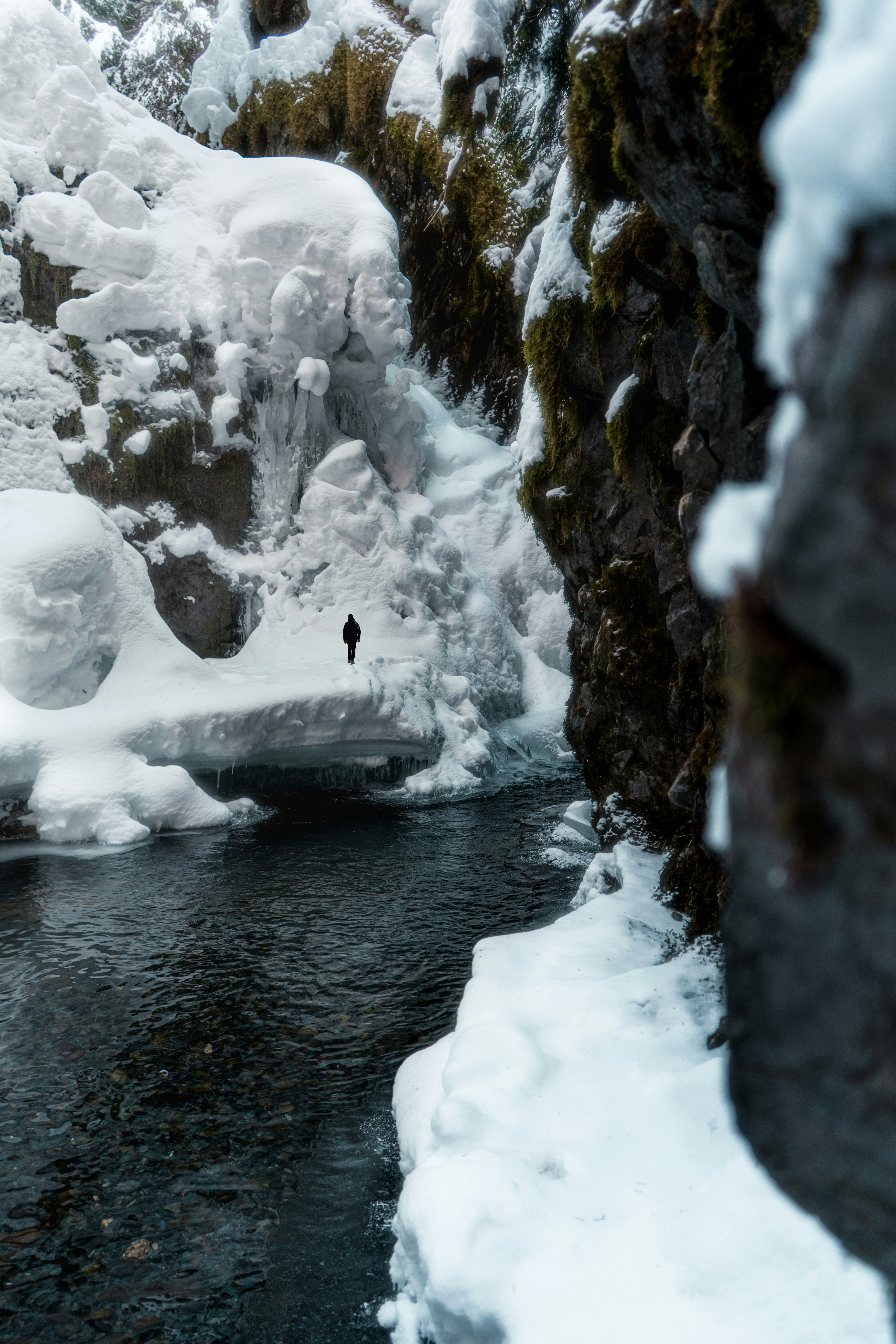 person in black jacket sitting on rock in river