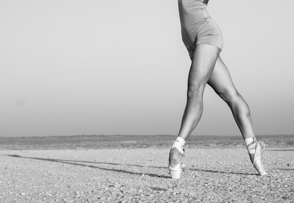grayscale photo of woman in white tank top and shorts walking on sand