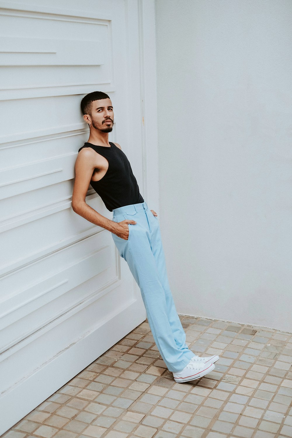 woman in black tank top and blue pants standing beside white wall