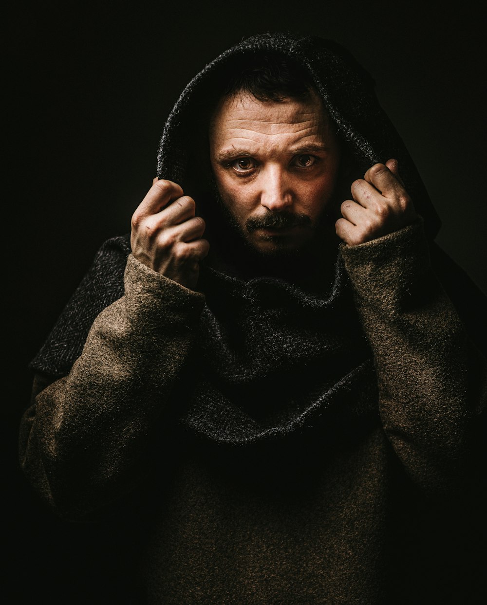 a man with a hoodie on holding his hands up to his face