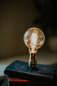 A stack of old philosophy and mathematics books with a glowing light bulb above them.