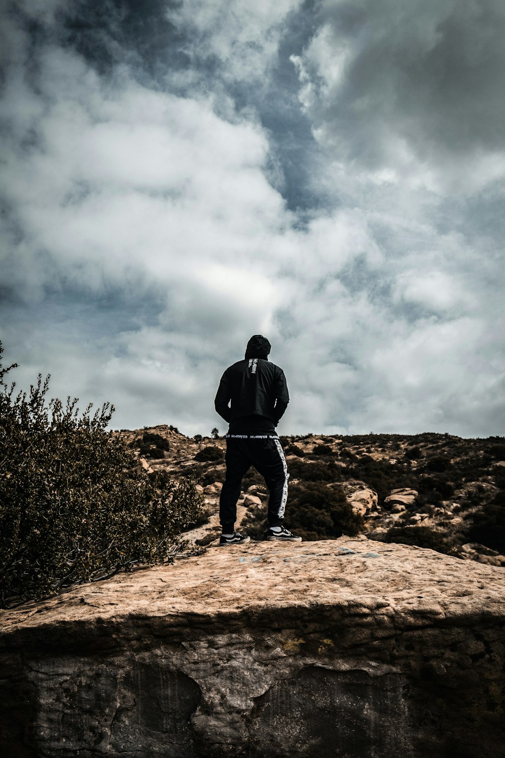 man in black jacket standing on brown rock under white clouds during daytime