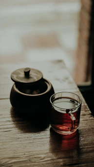 A rustic wooden table with a steaming herbal brew in a handcrafted clay cup, surrounded by fresh herbs and dried flowers.