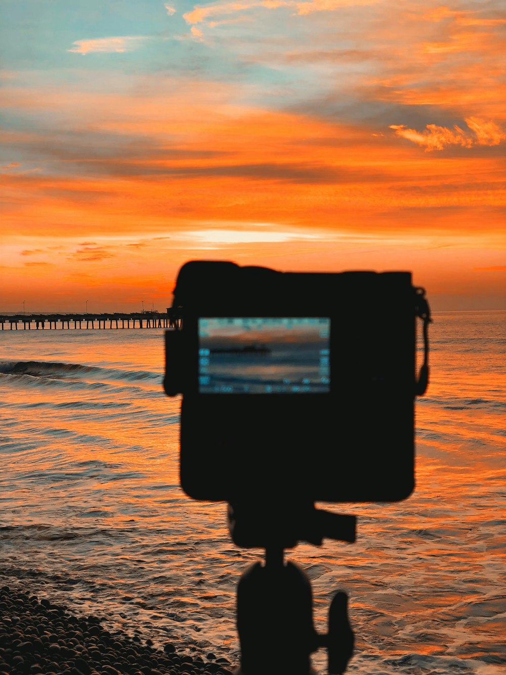 silhouette of camera taking photo of sea during sunset