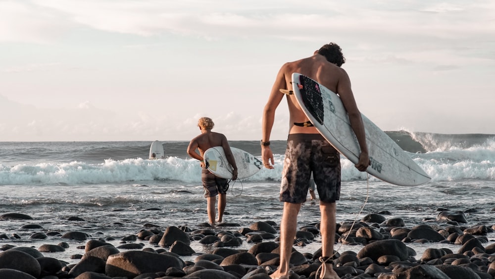 2 women holding surfboard standing on rocky shore during daytime