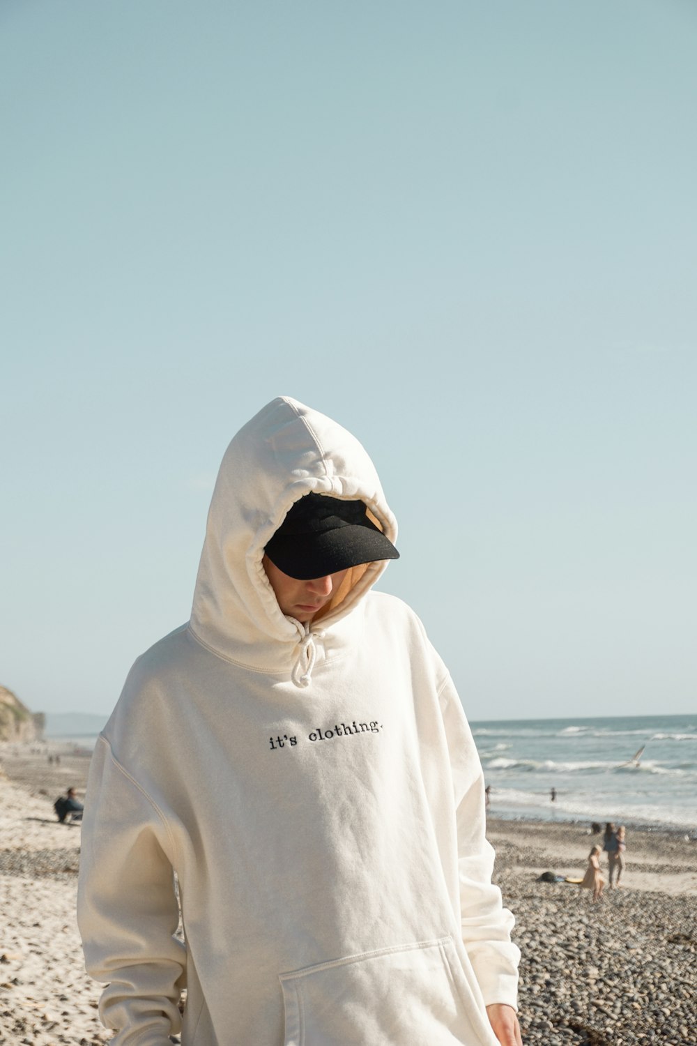 person in white hoodie wearing white cap standing on beach during daytime
