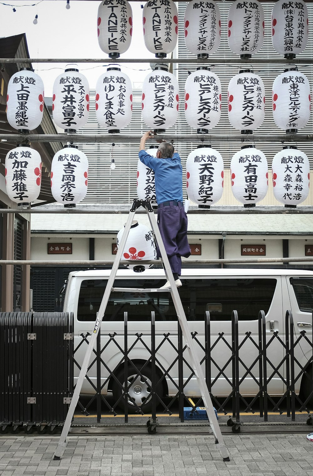 昼間、白い車のそばに立つ青いパーカーを着た男