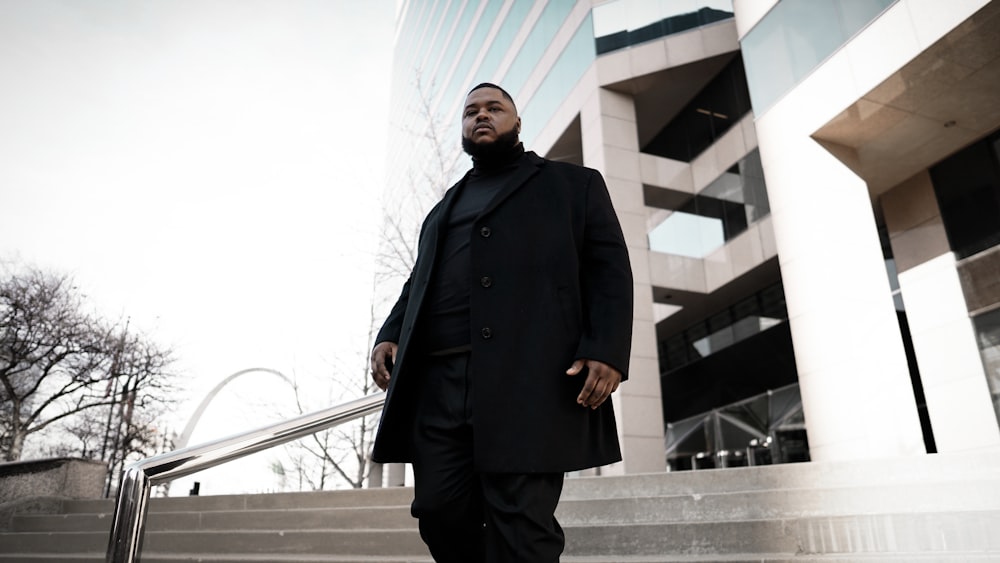 man in black coat standing on gray concrete stairs