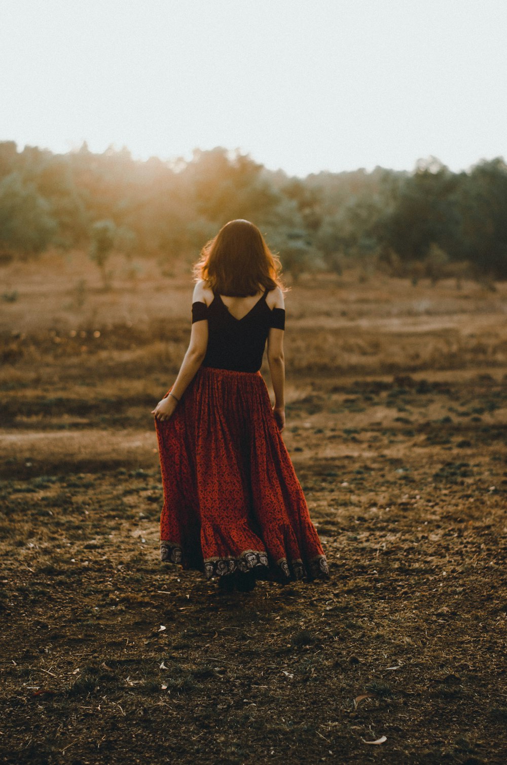 Mujer en vestido negro y rojo de pie en suelo de tierra durante el día