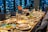 A dining table is elegantly set with diverse plates of food, including salads and entrees. Crystal glasses and cutlery are arranged alongside pitchers of beverages. The background features a window with a view of city lights, creating a cozy and sophisticated atmosphere.