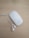 A white wireless computer mouse and a pair of white earphones rest on a light wooden surface. The mouse is sleek and glossy, with a minimalist design. The earphones are untangled, positioned next to the mouse, with their wires neatly laid out.