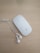 A white wireless computer mouse and a pair of white earphones rest on a light wooden surface. The mouse is sleek and glossy, with a minimalist design. The earphones are untangled, positioned next to the mouse, with their wires neatly laid out.