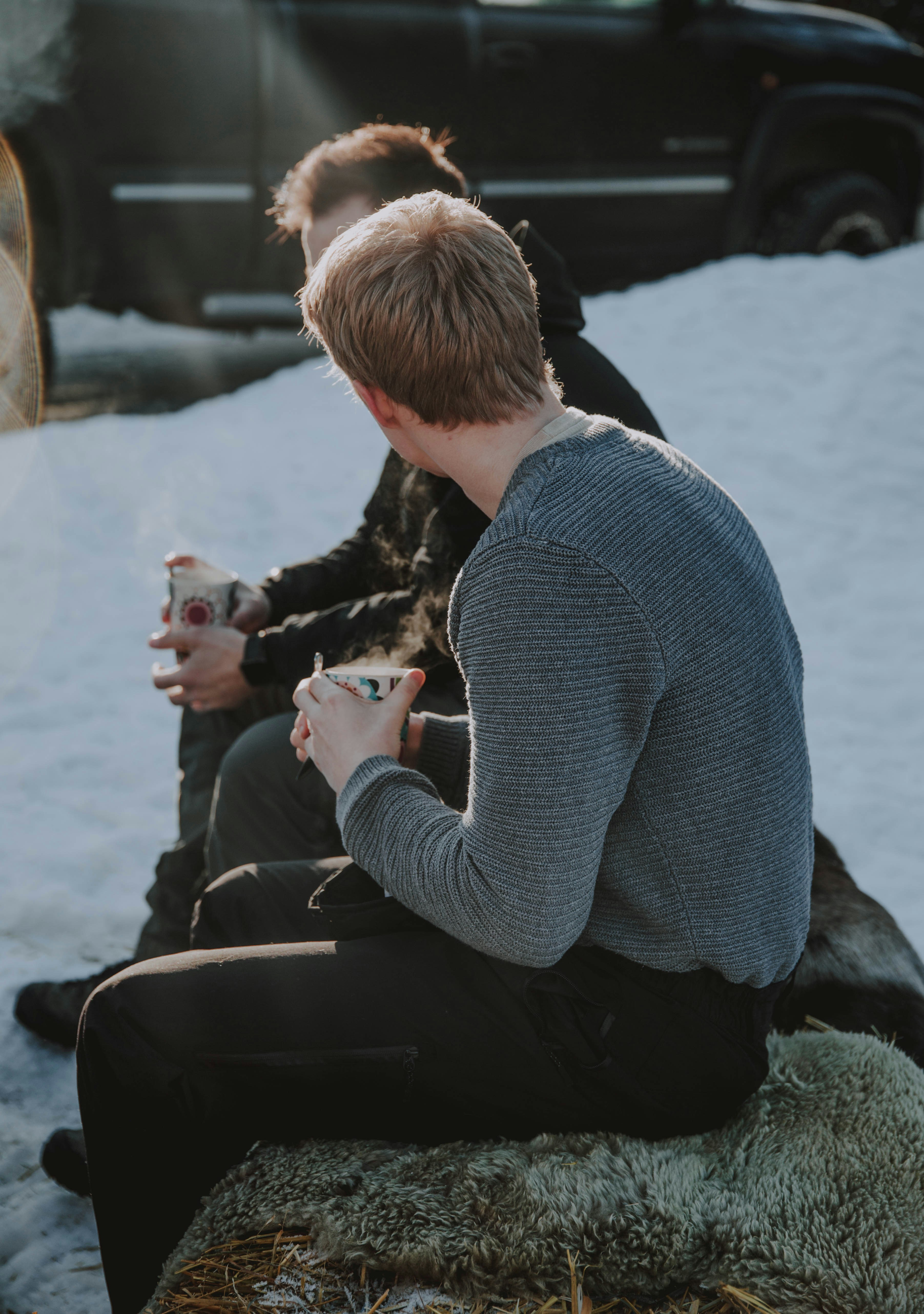 man in gray sweater sitting on rock while holding white cup