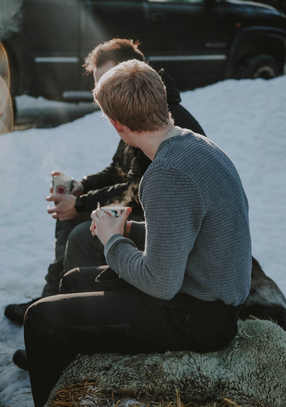 Mann in grauem Pullover sitzt auf Felsen und hält eine weiße Tasse in der Hand