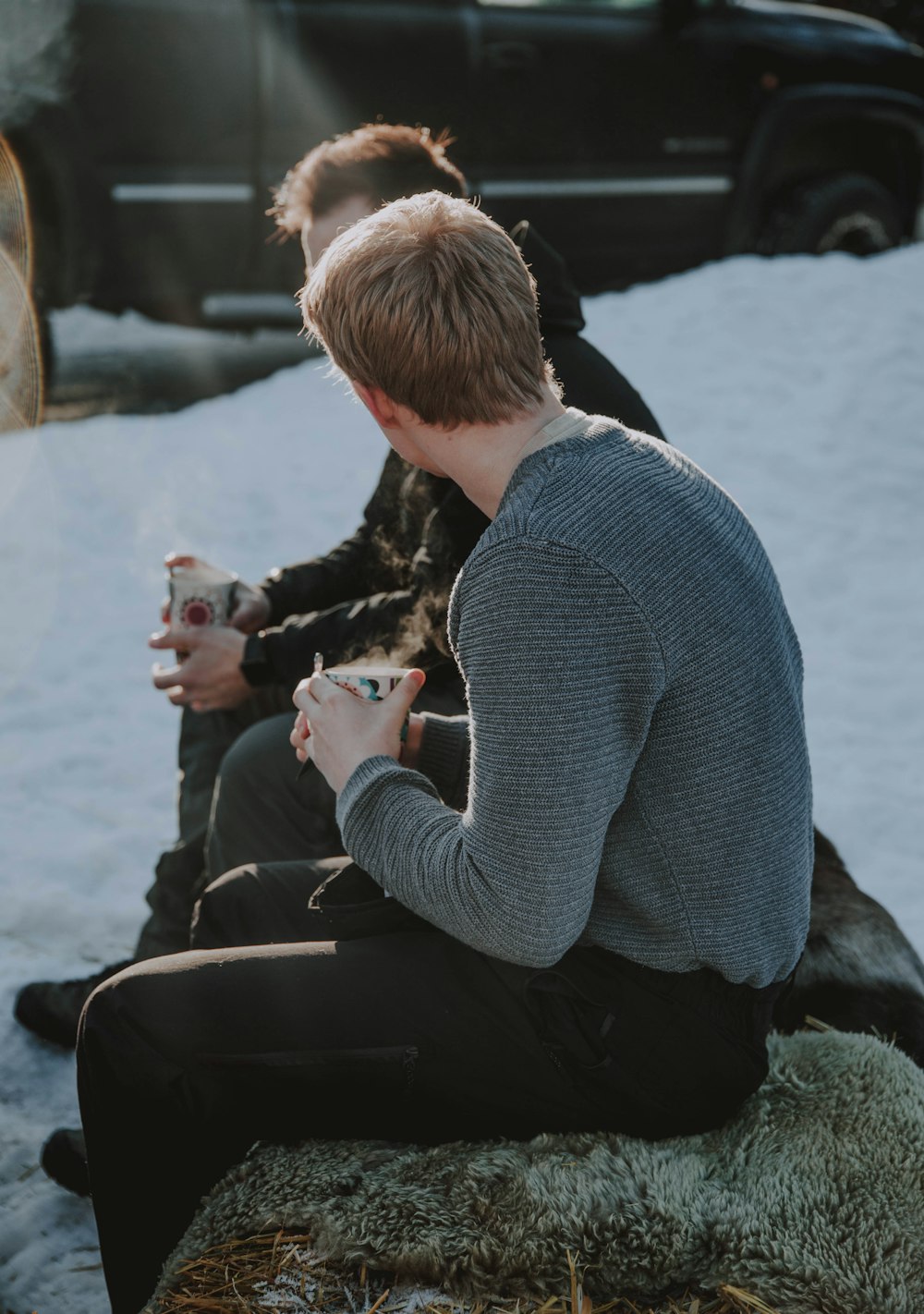 man in gray sweater sitting on rock while holding white cup