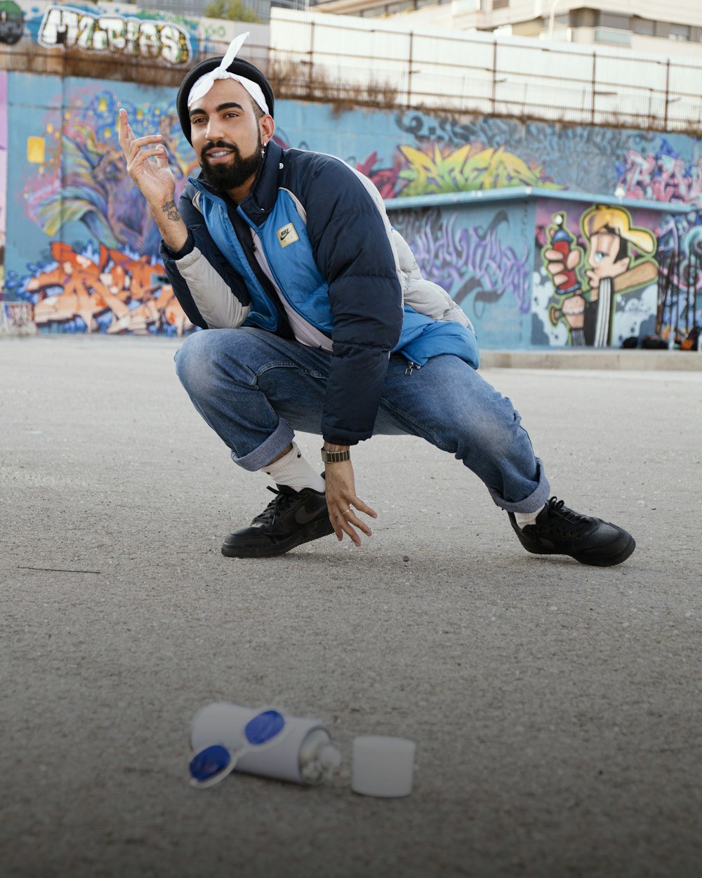 man in blue jacket and blue denim jeans sitting on gray concrete floor