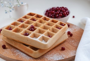 A whimsical shot of waffles stacked high with pistachio cream and dusted with powdered sugar against a sky blue background