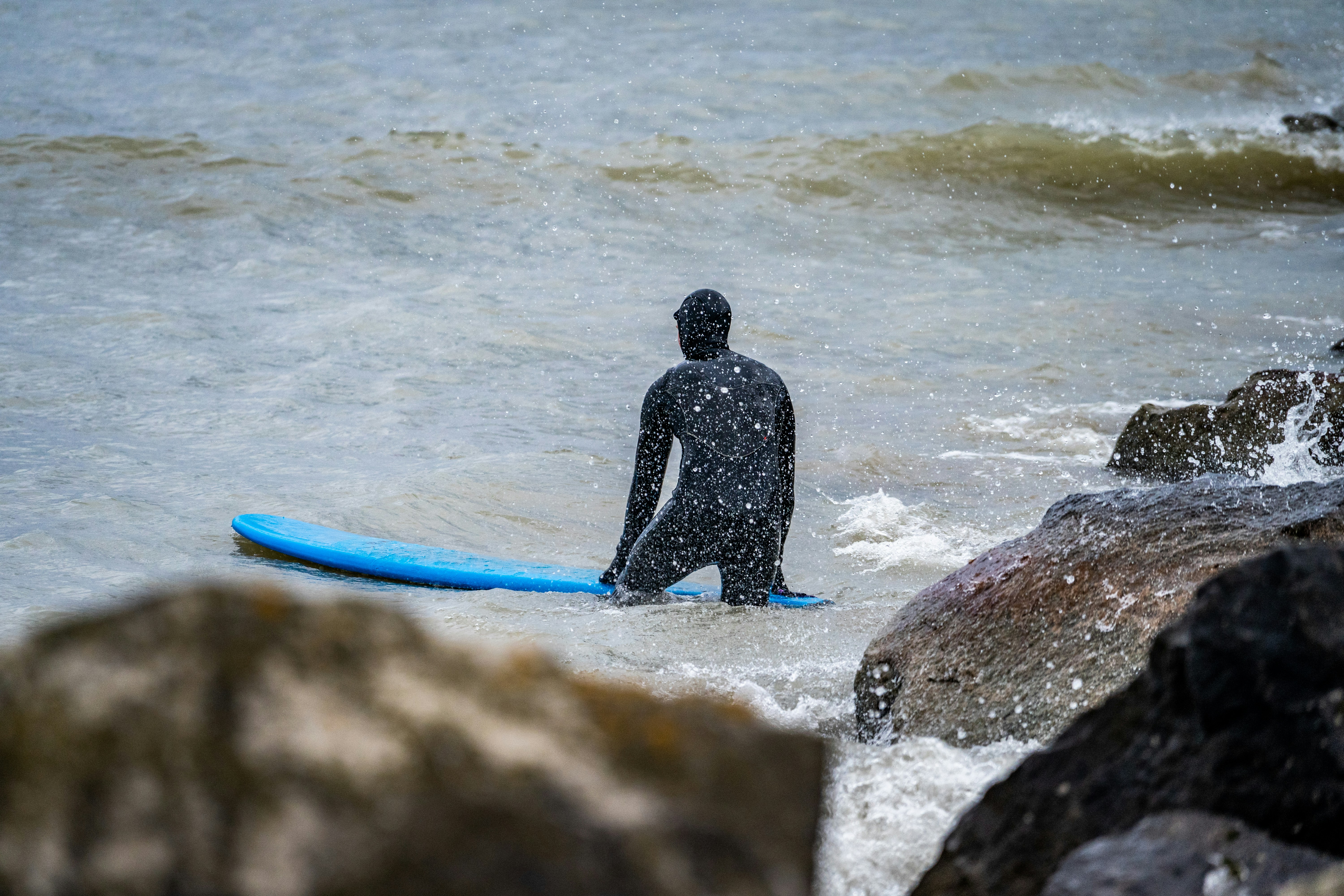 homme en combinaison noire tenant une planche de surf bleue marchant sur le bord de mer pendant la journée