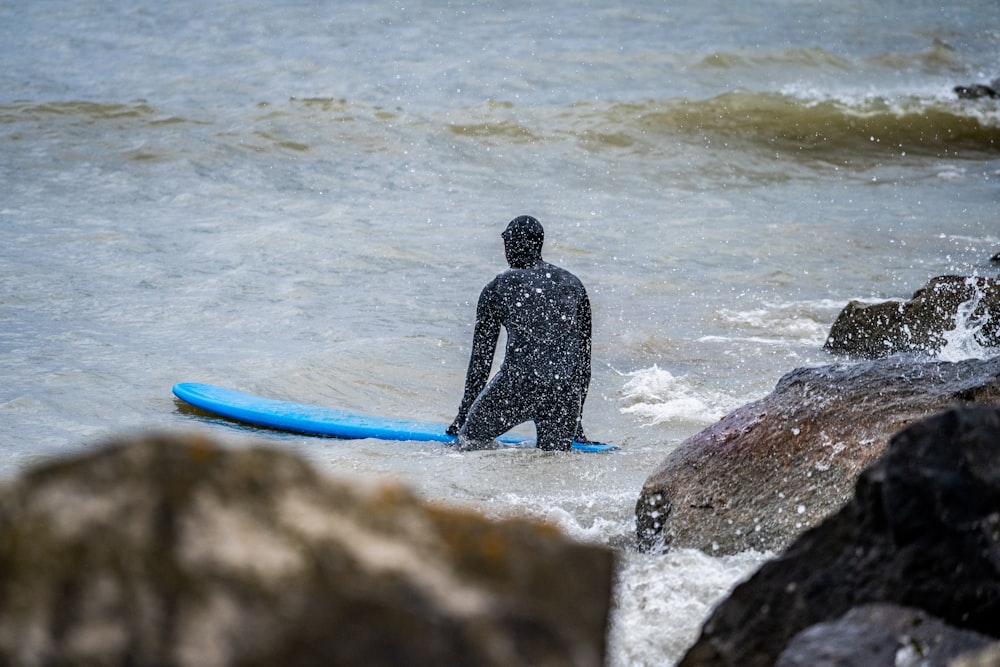 man in black wet suit holding blue surfboard walking on seashore during daytime