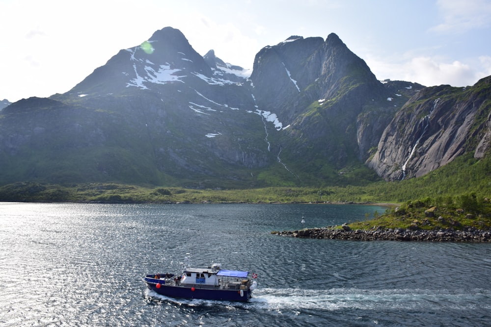 white and blue boat on water near mountain during daytime