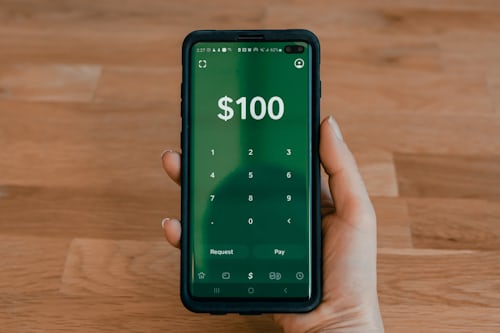 Smartphone preto exibindo a quantia de US$ 100 e um teclado numérico enquanto a pessoa se prepara para comprar seguidores do TikTok.