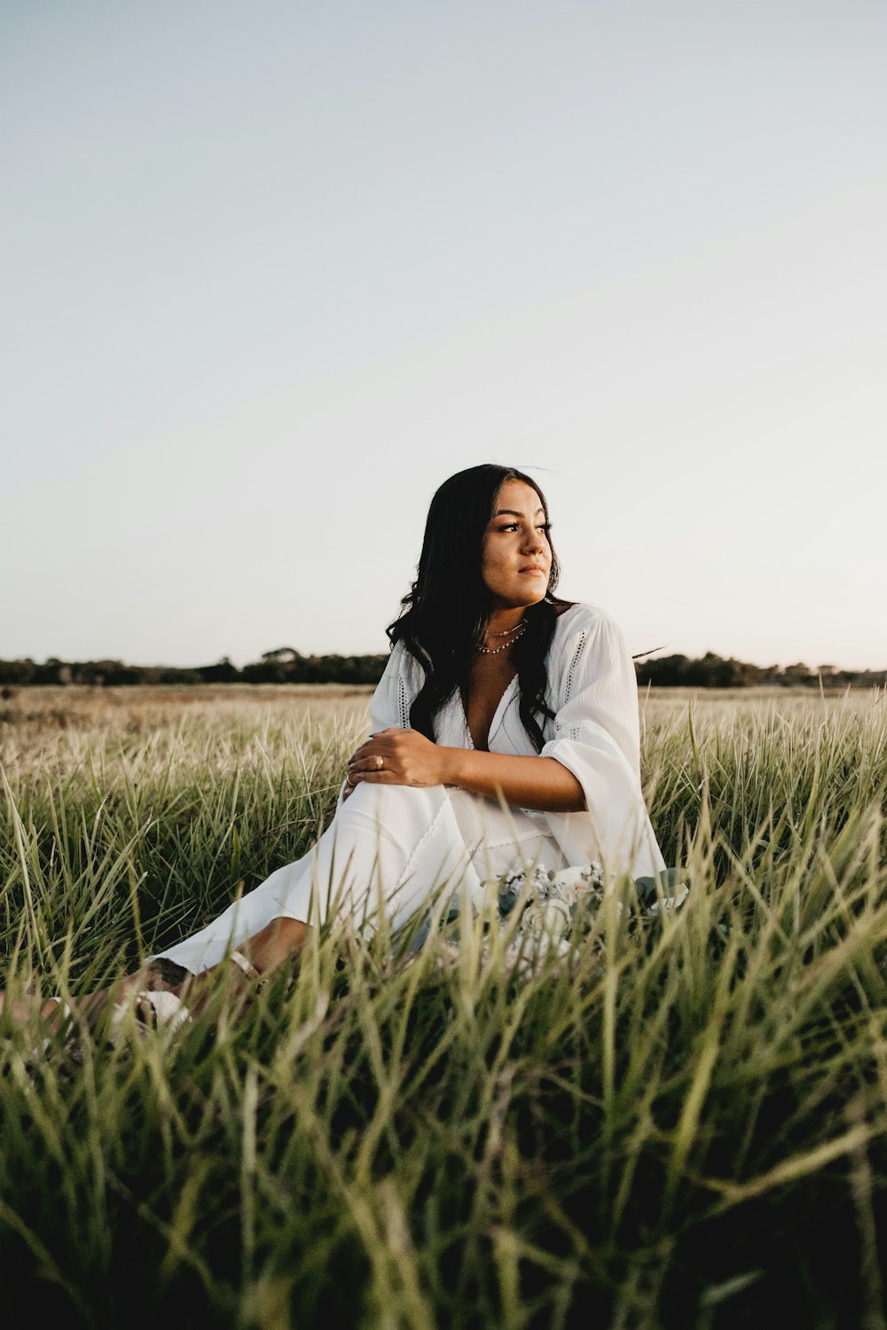 femme en robe blanche assise sur le champ d’herbe verte pendant la journée