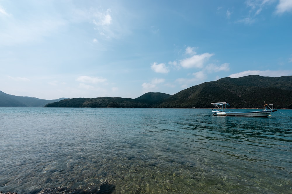 barca bianca sul mare vicino alla montagna verde sotto il cielo blu durante il giorno