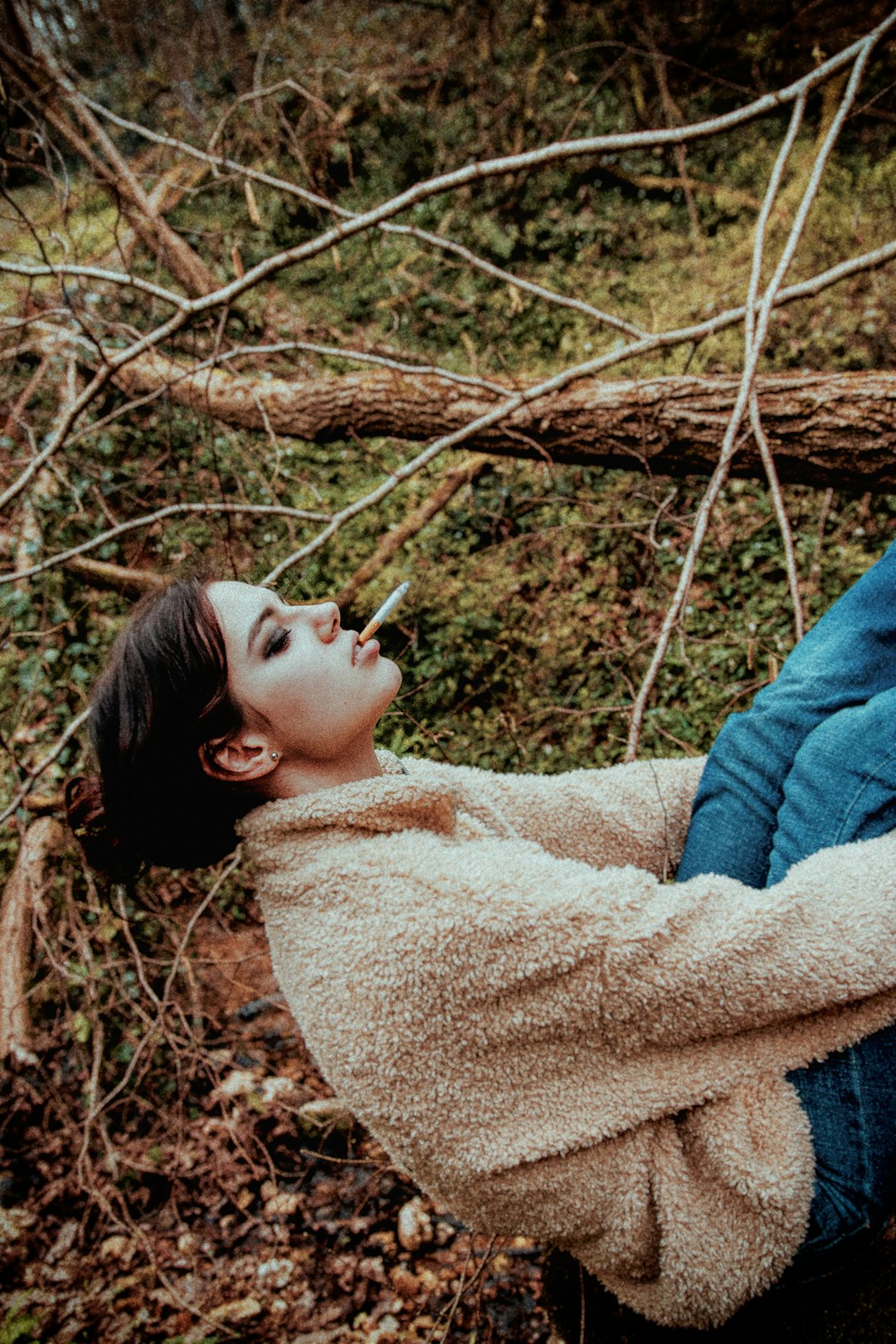 woman in brown sweater lying on brown dried leaves during daytime