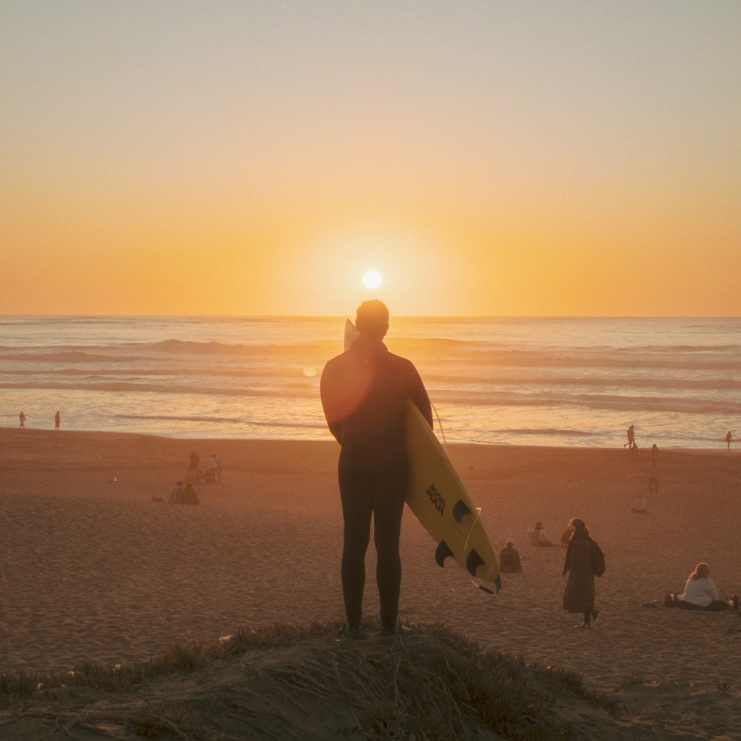 silhouette of man holding surfboard walking on beach during sunset