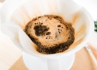 Close-up of a frothy filter coffee being poured from a stainless steel pot.