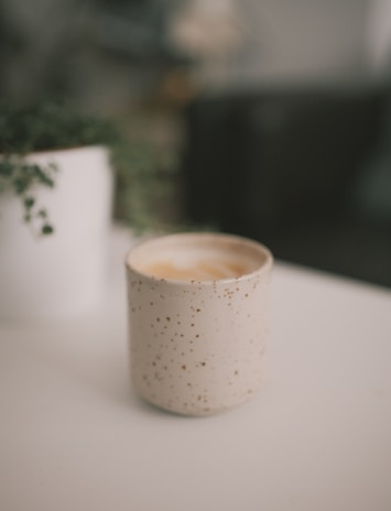 A white ceramic mug with a subtle design next to a small potted plant on a cozy desk.