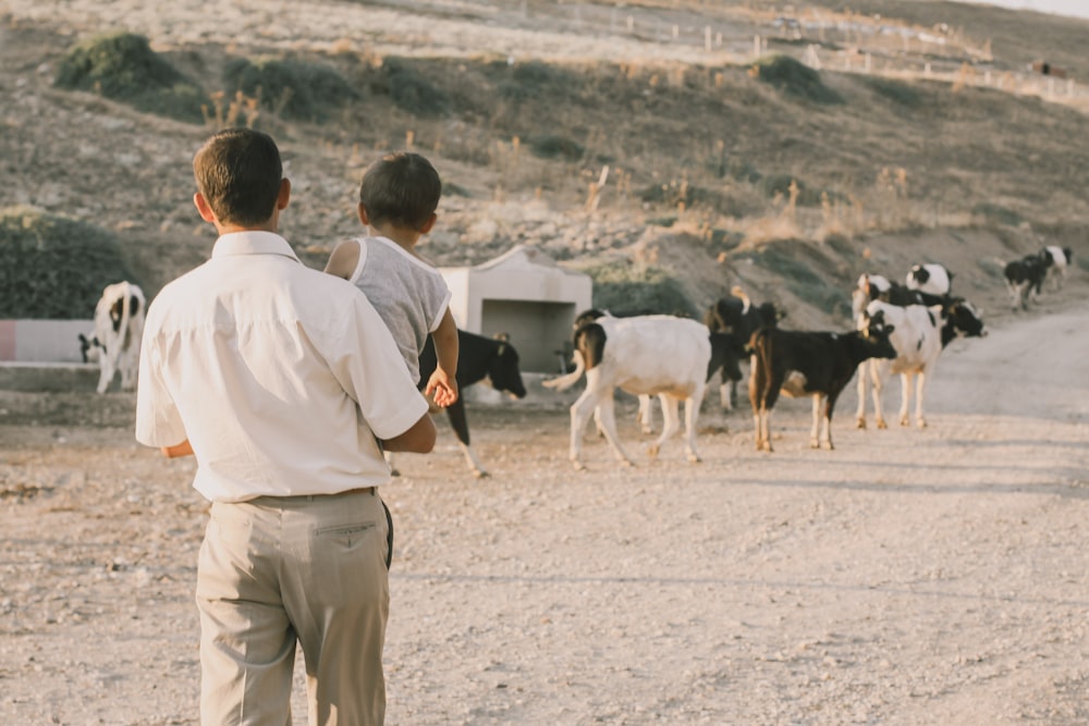 man in white dress shirt standing beside black and white cow during daytime