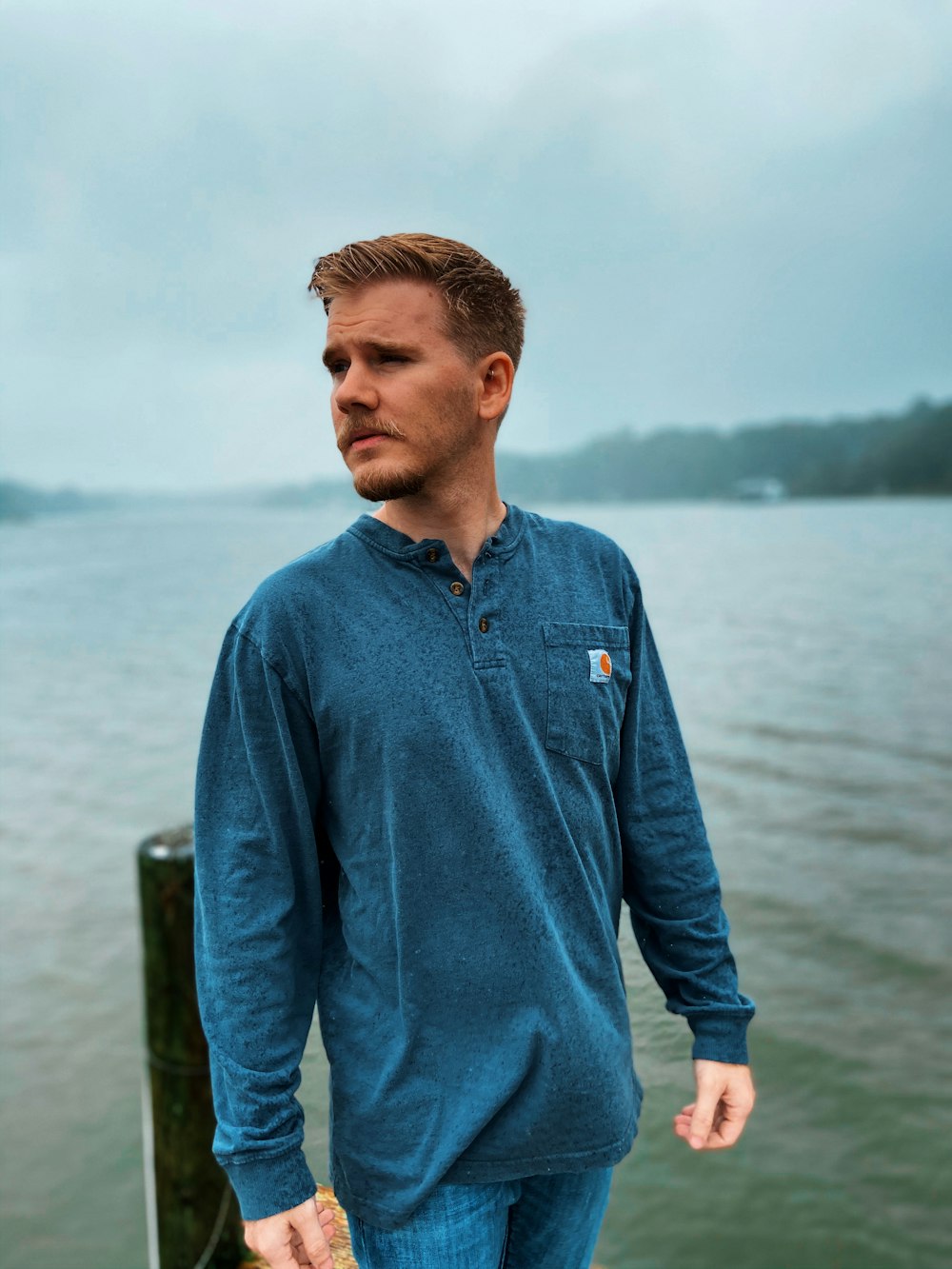 man in blue dress shirt standing near body of water during daytime
