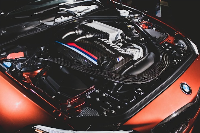 A detailed view of a car engine featuring sleek components and a cover marked with 'MPower'. The image highlights a mix of metallic textures and intricate details of the engine's design. The surrounding parts are well-organized with visible branding elements.