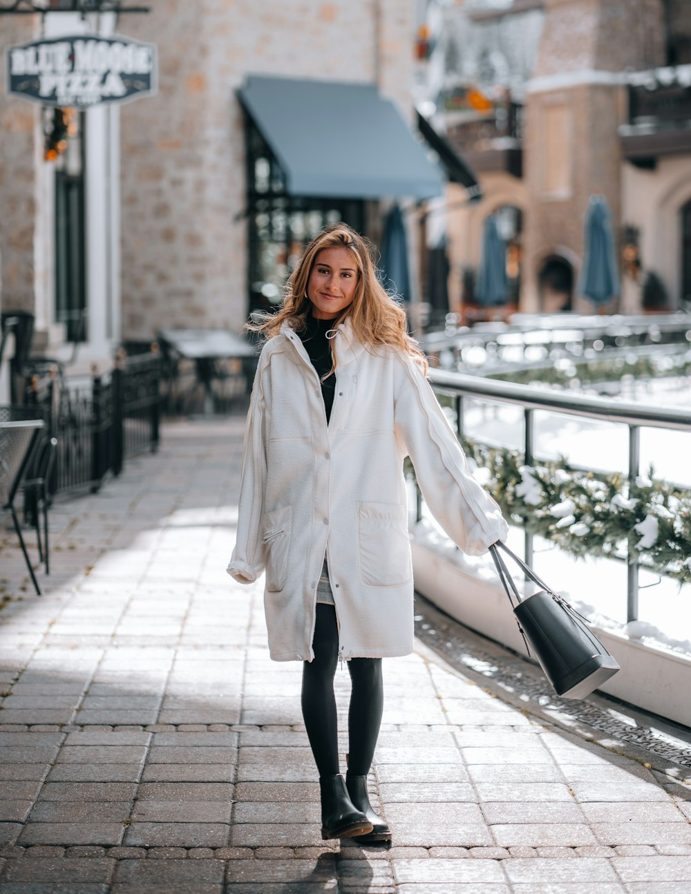 woman in white coat standing on sidewalk during daytime