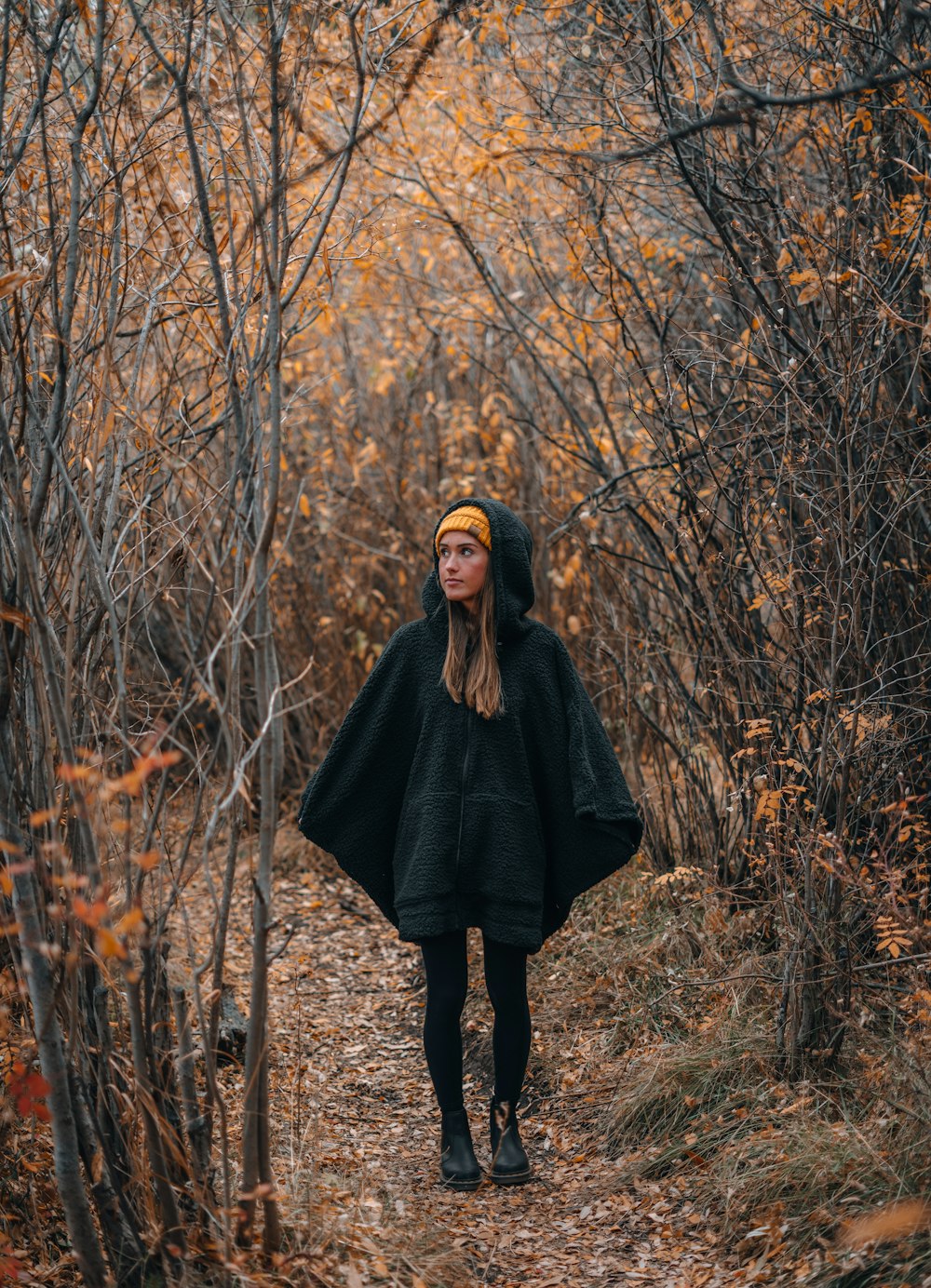 femme en manteau noir debout sur le champ d’herbe brune pendant la journée