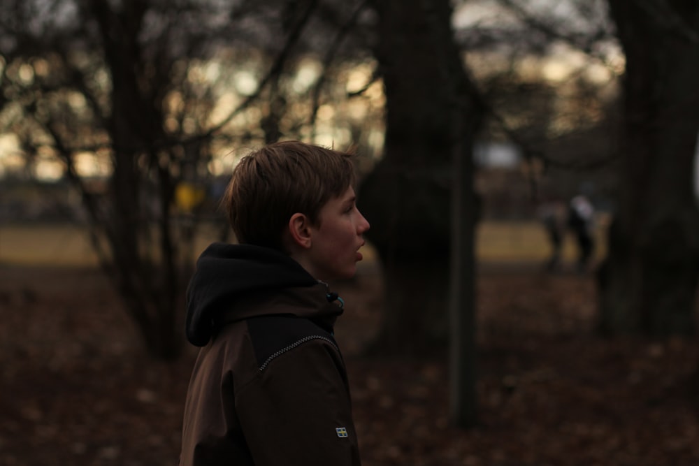 boy in black hoodie standing near trees during daytime