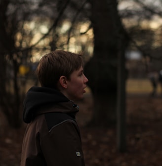 boy in black hoodie standing near trees during daytime