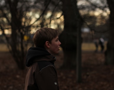 boy in black hoodie standing near trees during daytime