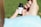 A person's hands are holding a small bottle labeled with 'NuLeaf' and 'Δ8THC'. The person's thumb and index finger are gripping the bottle while the other hand's fingers are visible in the background. The background is blurred and appears to be a grassy area.