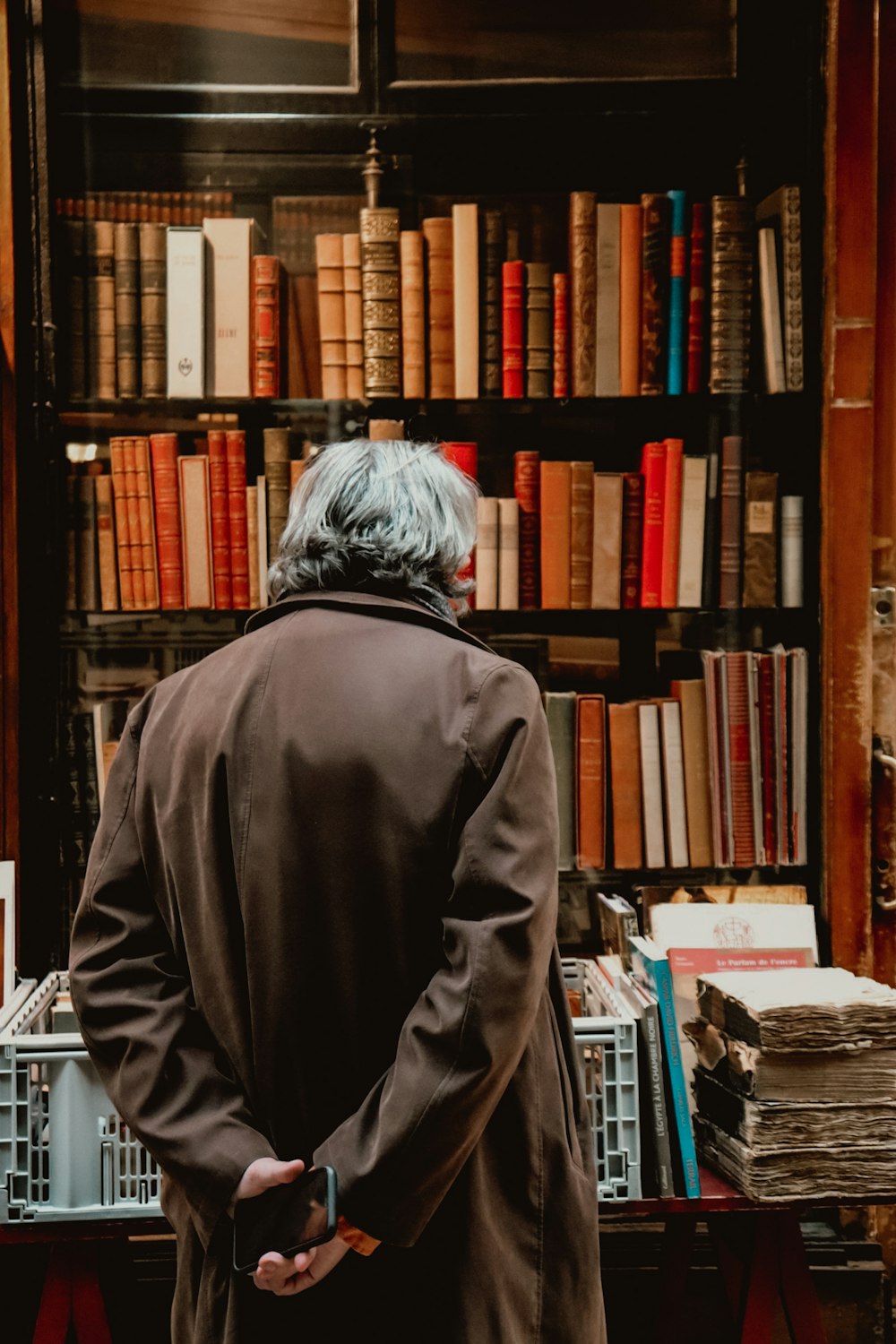 Persona in felpa grigia con cappuccio in piedi vicino ai libri