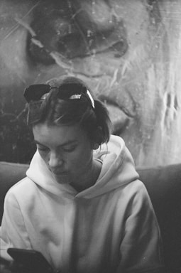 A sleek black and white photo of a streetwear-clad young man texting on his phone against an urban backdrop.