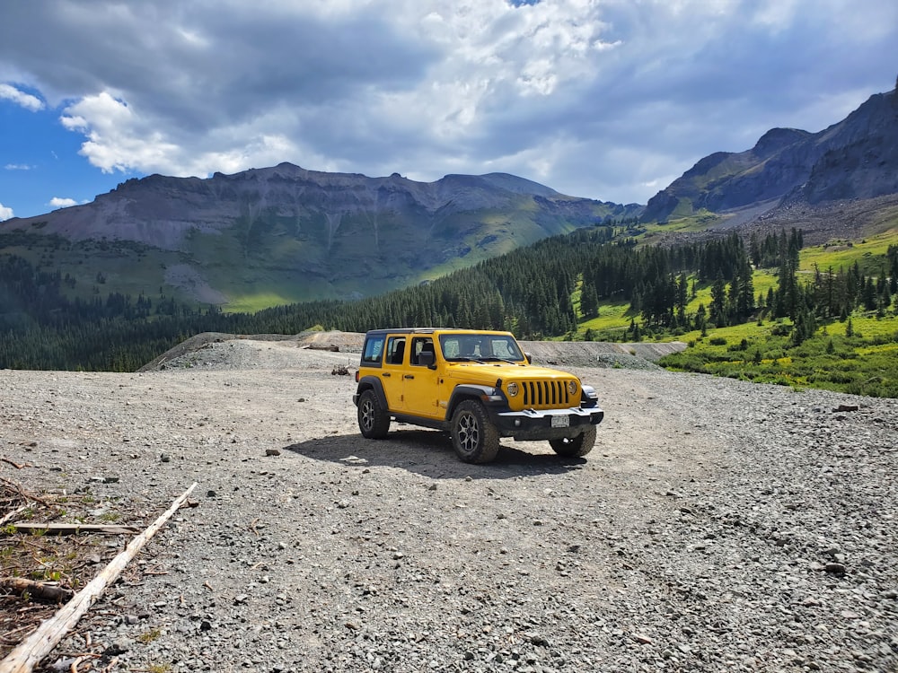 yellow and black jeep wrangler on dirt road near green trees during daytime