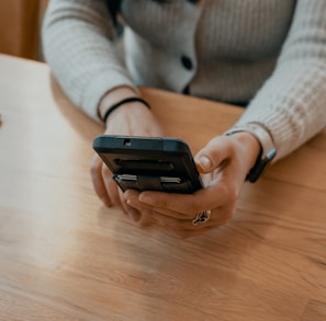 woman in white sweater holding black smartphone